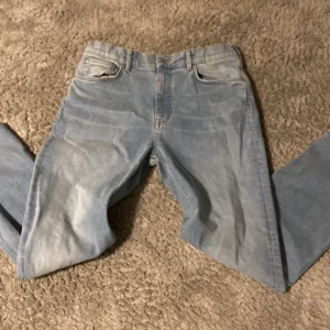 Ljusblå jeans från GANT - Säljer ett par ljusblå jeans från GANT i storlek 158/164 cm, passande för åldern 13-14 år. Byxorna har en klassisk femficksdesign och en läderpatch med GANT-loggan på baksidan. Perfekta för en avslappnad stil.