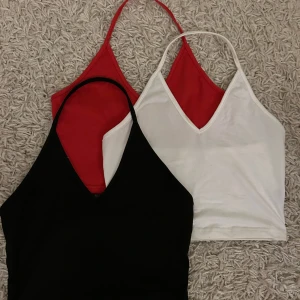 Tre halterneck linnen i olika färger - Säljer tre snygga halterneck linnen i svart, rött och vitt. Perfekta för sommaren med en stilren v-ringad design. De är ärmlösa och har en bekväm passform. Passar bra till både jeans och kjol. Aldrig använda! Fraktar endast varan och köparen betalar frakten! Priset som syns är vad som gäller🙏🫶