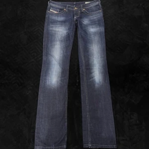 Blå jeansbyxor från Diesel - Snygga blå jeansbyxor från Diesel med en klassisk femficksdesign och guldfärgade knappar. Byxorna har en lätt slitning på framsidan för en trendig look. Perfekta för en avslappnad stil. 25/32