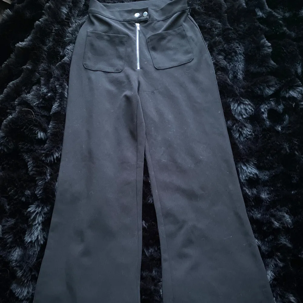 Snygga svarta byxor från Bik Bok med hög midja och vida ben. Byxorna har en dragkedja och knappar framtill samt praktiska fickor. Perfekta för en stilren look.. Farkut & Housut.