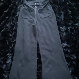 Svarta byxor från Bik Bok - Snygga svarta byxor från Bik Bok med hög midja och vida ben. Byxorna har en dragkedja och knappar framtill samt praktiska fickor. Perfekta för en stilren look.