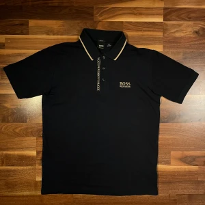 Navy blå pikétröja från Hugo Boss - Säljer en stilren navy blå pikétröja från Hugo Boss med beige detaljer på kragen och knäppningen.                                                               Pris kan diskuteras vid snabb affär✅👌🏼