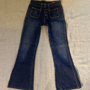 Mörkblå jeans med knappar - Snygga mörkblå jeans från Brappers med en klassisk bootcut-stil. De har en hög midja och knappar framtill. Perfekta för en avslappnad look med en touch av retro. Midjemått: 36cm. Innerbenslängd: 75cm