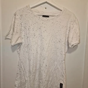 Vit t-shirt från Things to Appreciate - Snygg vit t-shirt från Things to Appreciate med ett coolt svart stänkmönster. Garderobsrensning så kika gärna på övriga.