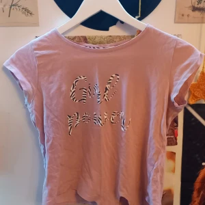 Rosa t-shirt med 'Girl Power'-tryck - Säljer en rosa t-shirt med texten 'Girl Power' i ett coolt mönster. T-shirten har korta ärmar och en avslappnad passform. Perfekt för en casual look!