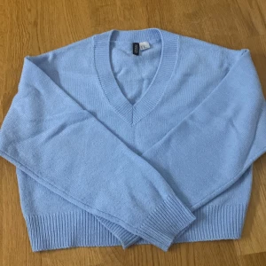 Ljusblå stickad tröja från H&M Divided - Säljer en ljusblå stickad tröja från H&M Divided. Tröjan har en v-ringad hals och långa ärmar med ribbade muddar. Säljer för att jag inte andvönder längre