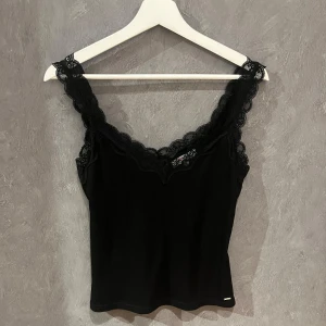 Svart linne med spetsdetaljer - Snygg svart linne med spetsdetaljer längs axelbanden och halsringningen. 