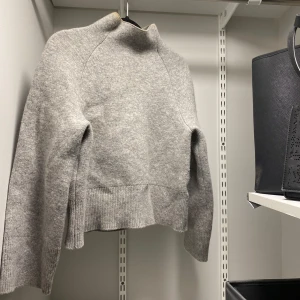 Grå ullblandad tröja från H&M - Säljer en stilren grå tröja från H&M i ullblandning. Tröjan har en hög krage och långa ärmar, perfekt för kyligare dagar. Den är mjuk och bekväm, idealisk för både vardag och mysiga stunder hemma. Storlek xs