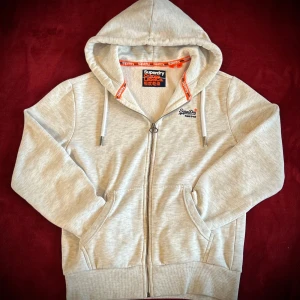 Grå hoodie från Superdry - Säljer en stilren grå zip hoodie från Superdry. Tröjan är väldigt sparsamt använd och har då inga defekter som skador eller fläckar. Priset går att diskutera vid snabb affär, vid minsta fråga eller fundering är det bara att höra av sig🤩😄