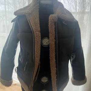 Brun jacka med foder från Bershka - Säljer en brun jacka från Bershka med mysigt brunt foder. Jackan har en cool bikerstil med dragkedjor och en stor krage. Perfekt för kyliga dagar när du vill hålla stilen. Aldrig använt. (pris går att diskutera)