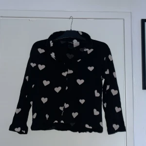 Pyjamaströja - En svart pyjamaströja med ljusrosa hjärtan. Den har knappar från toppen till botten. Skönt material. 