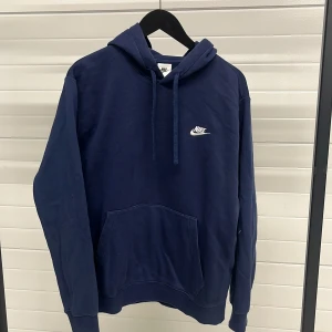 Mörkblå hoodie från Nike - Säljer en stilren mörkblå hoodie från Nike med klassisk logga på bröstet. Hoodien har en stor ficka framtill och justerbar huva med dragsko. Perfekt för en avslappnad look.