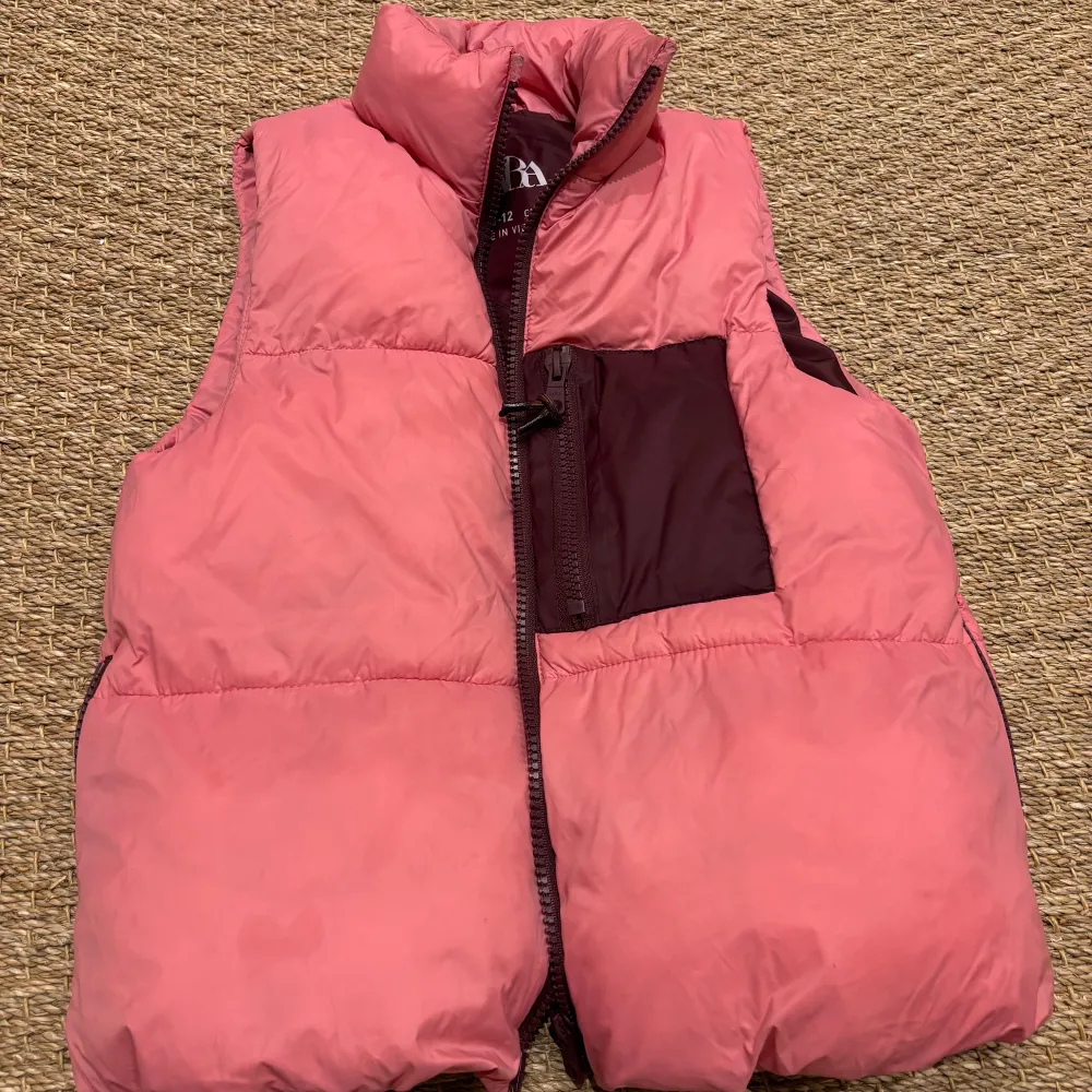 Säljer en snygg rosa dunväst från Zara i storlek 11-12 år. Västen har en dragkedja framtill och en praktisk ficka i mörkare nyans. Perfekt för kyliga dagar och ger en cool look. Passar bra till både vardag och utflykter.. Jackor.