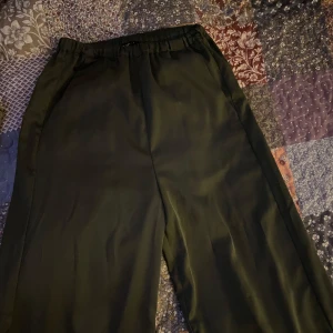 Gröna kostym byxor från Lindex - Säljer ett par gröna kostymbyxor  från Lindex i storlek XS. De har en loose och bekväm passform med elastisk midja. Perfekta för både vardag och festliga tillfällen. Har använts fåtal gånger 