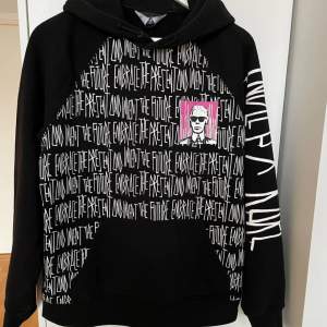 Cool svart hoodie med texten 'Embrace the Present and Move the Future' i vitt över hela framsidan och baksidan. Har en stor grafisk bild av en person i solglasögon på både fram- och baksidan. Perfekt för en avslappnad stil och att sticka ut i mängden. Nypris 3000kr