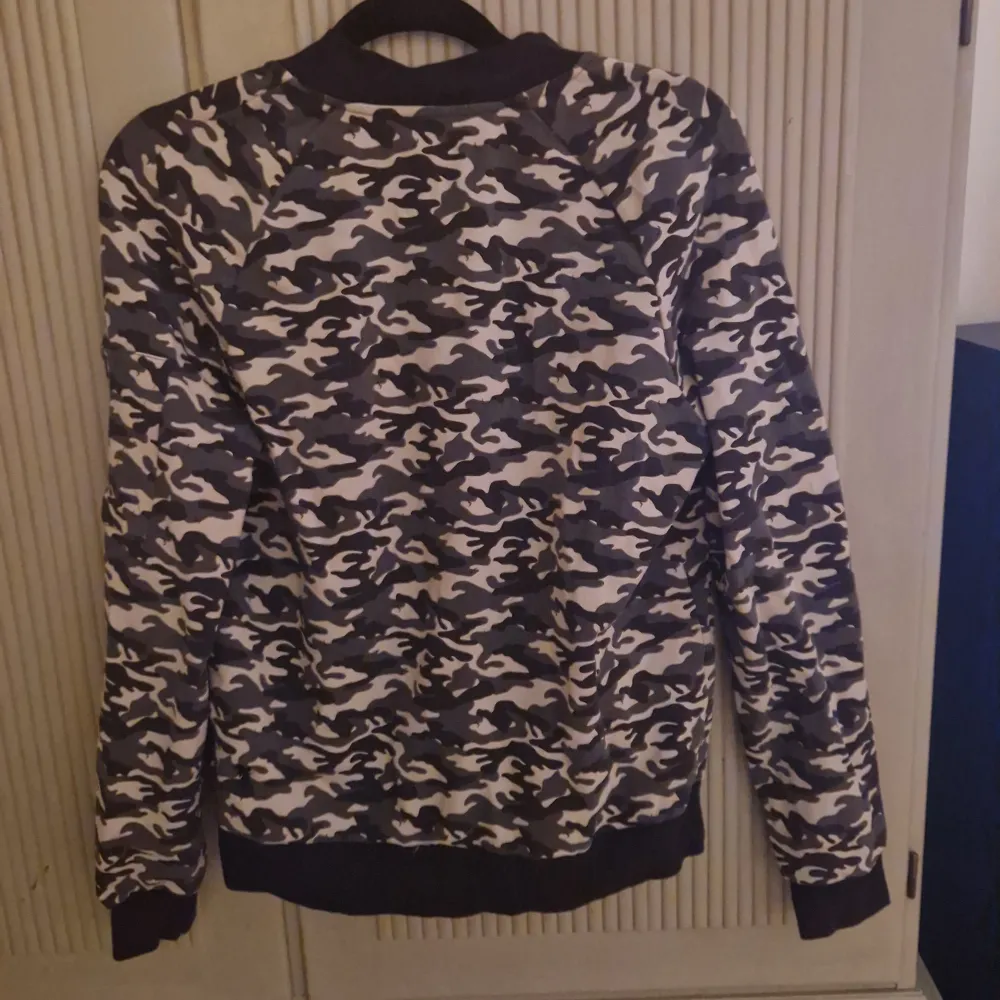 Säljer en snygg bomberjacka i camouflage från House of Lola. Jackan har en dragkedja framtill och är långärmad med ribbade muddar. Perfekt för en cool och avslappnad stil. Passar bra till både höst och vår!. Tröjor & Koftor.