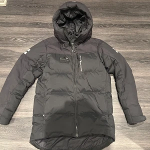 Sail Racing vinterjacka - Säljer en svart dunjacka från Sail racing i ny skick. Den har en praktisk huva och dragkedja framtill. Perfekt för kalla vinterdagar. Jackan är långärmad och har en stilren design. Passar både till vardags och utomhusaktiviteter. Denna jacka är knappt använd och när som ny. Köpte den för ca 1 år sedan för 4200kr från stadium och har knappt använt den. (Storleken är S men passar även perfekt för M) Skriv för mer info!