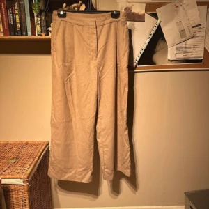 Beige byxor från Monki - Säljer ett par snygga beige byxor från Monki i storlek 38. De har en stilren design med dragkedja och knapp framtill. Perfekta för både vardag och fest! 🕺