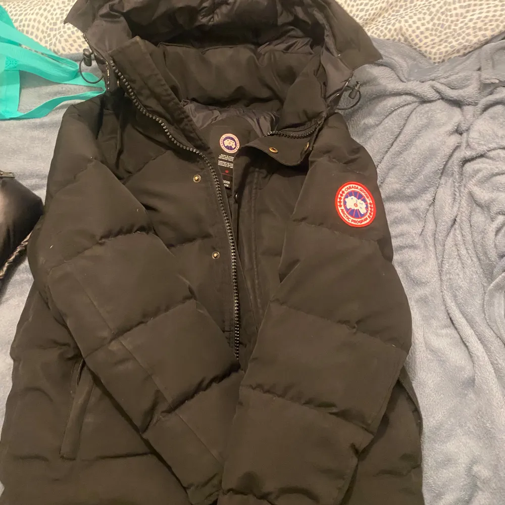 Säljer en svart dunjacka från Canada Goose i mycket bra skick. Jackan har en klassisk design med dragkedja och knappar, perfekt för kalla vinterdagar. Den är varm och bekväm med en snygg logga på ärmen. Passar perfekt för vinterns alla äventyr! ❄️. Jackor.