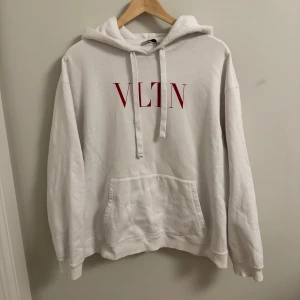 Valentino Hoodie - Säljer en stilren vit hoodie med röd VLTN-logga på bröstet. Den är superbekväm och perfekt för både chill och vardagsäventyr. Har en klassisk känguruficka och justerbar huva. Passar perfekt till jeans eller joggers!