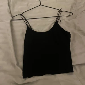 Svart ärmlös linnetopp - Säljer en enkel och stilren svart linnetopp med smala axelband. Perfekt för sommardagar eller som ett basplagg i garderoben. Toppen är i bra skick och passar till många olika outfits.