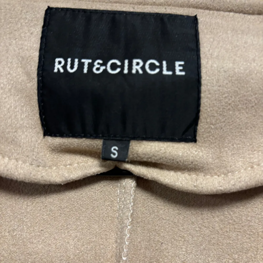 Säljer en stilren beige kappa från Rut & Circle i storlek S. Den har långa ärmar och snygga knapplister på axlarna. Perfekt för höst och vår, med en klassisk design som passar till allt. Kappan är i mycket bra skick och redo för nya äventyr!. Jackor.