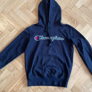 Mörkblå hoodie från Champion - Säljer en snygg mörkblå hoodie från Champion i mycket bra skick. Den har en klassisk Champion-logga på bröstet och en praktisk magficka. Perfekt för höst och vår, eller när du bara vill chilla hemma. Passar både till träning och vardagsoutfits. 🏆