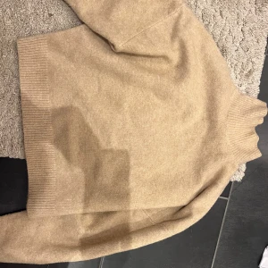 Beige stickad polotröja - Mysig beige stickad polotröja i mycket bra skick. Perfekt för kyliga höst- och vinterdagar. Tröjan har långa ärmar och ribbade detaljer vid ärmslut och nederkant. En klassisk och stilren design som passar till det mesta.