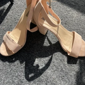 Beige sandaler med klack - Säljer ett par snygga beige sandaler med klack. De har en öppen tå och en bekväm rem runt ankeln. Perfekta för sommarens fester eller en dag på stan. Använda men i bra skick, med lite slitage på sulorna.