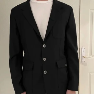 Svart kavaj - Säljer en stilren svart kavaj i herrstorlek. Den har tre knappar framtill och klassiska fickor. Perfekt för både formella och semi-formella tillfällen. Passar bra över en vit t-shirt för en mer avslappnad look.