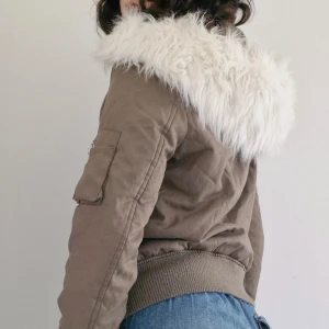 Y2K bomberjacka - Supersnygg bomberjacka från Glam Amour! 🎀 Khakifärgad med stor vit pälsluva och markerad midja. Hela huvan kan tas av med dragkedja, eller enbart pälsen med knappar. Finns en liten fläck på ärmen, se sista bilden. Bara o fråga om ni undrar något! 
