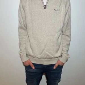 Beige tröja med dragkedja från Bondelid - Snygg beige tröja från Bondelid med dragkedja och broderad logga på bröstet. Perfekt för en avslappnad stil. Tröjan har långa ärmar och ribbade muddar vid ärmslut och nederkant.