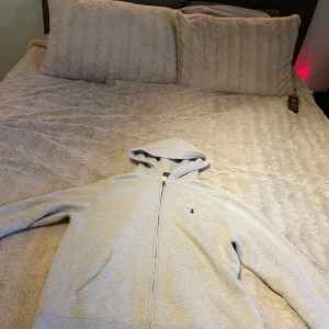 Grå hoodie från Ralph Lauren - Säljer en stilren grå hoodie från Ralph Lauren med dragkedja och klassisk logga på bröstet. Perfekt för en avslappnad look. Den har långa ärmar och en bekväm passform. I princip helt ny använd max 3 gånger. Pris kan diskuteras.