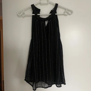 Svart ärmlös topp med gulddetaljer - Snygg svart ärmlös topp från bikbok med gulddetaljer längs hela toppen. Perfekt för en kväll ute eller en speciell tillställning. Toppen har en elegant design med en liten öppning vid halsen.