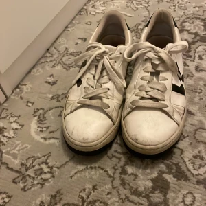 Vita sneakers från Kenzo - Säljer ett par vita sneakers från Kenzo med svarta detaljer och snörning. Skorna har en klassisk design med märkets logga på hälen.