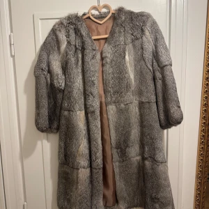 Grå pälsjacka  - Elegant grå pälsjacka med halv långa ärmar och knäppning framtill. Jackan har en mjuk och lyxig känsla, perfekt för kyliga dagar. Den har en brun insida som ger en fin kontrast till den grå utsidan. Använd 2 ggr