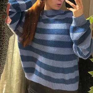 Blårandig stickad tröja - Säljer en mysig stickad tröja i blå och mörkblå ränder. Tröjan har en avslappnad passform med långa ärmar och ribbade muddar. Perfekt för kyliga dagar!