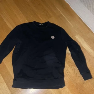 Svart tröja från Moncler - Snygg svart tröja från Moncler med broderad logga på bröstet. Perfekt för en stilren look. Tröjan har långa ärmar och rund halsringning.