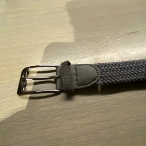 Grått flätat bälte - Snyggt grått flätat bälte med silverfärgat spänne. Perfekt för att ge en stilren touch till din outfit.