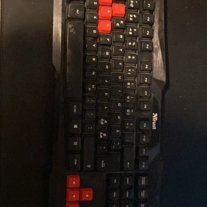 Svart och röd gamingtangentbord från Trust - Säljer ett gamingtangentbord från Trust med svart bas och röda detaljer på vissa tangenter. Perfekt för gaming med en robust design och tydliga markeringar på tangenterna. Ansluts via USB och har en klassisk layout. Bara för 100kr