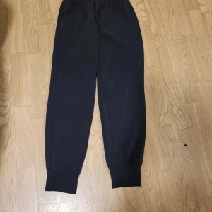 Svarta mjukisbyxor - Säljer ett par svarta mjukisbyxor i bekvämt material. Perfekta för en avslappnad dag hemma eller på språng. Byxorna har elastiska muddar vid bensluten för en skön passform.