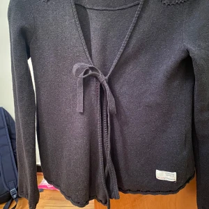 Mörkgrå kofta från Odd Molly - Säljer en stilren mörkgrå kofta från Odd Molly med knytband framtill. Perfekt för lager-på-lager och har en fin detalj med broderad etikett. Passar bra till både vardag och speciella tillfällen.