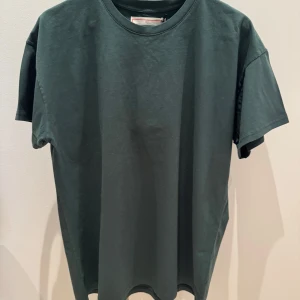 Mörkgrön t-shirt från Jeanerica - Snygg mörkgrön t-shirt från Jeanerica i 100% ekologisk bomull. Perfekt för en avslappnad stil med sin klassiska passform och korta ärmar. Enkelt och stilrent plagg för alla tillfällen. Oanvänd med etiketten kvar på plagget. Nypris 800kr