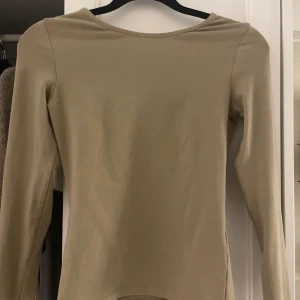 Beige/Grön långärmad topp med öppen rygg - Snygg beige/grön långärmad topp med en djup öppen rygg från NAKD. Stor i storleken, är vanligt vid en Xs-S
