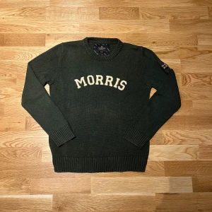 Mörkgrön stickad tröja från Morris - Säljer en snygg grön stickad tröja i storlek S från Morris med texten 'MORRIS' i vitt på bröstet. Tröjan har långa ärmar och ribbade muddar vid ärmslut och nederkant. Perfekt för kyligare dagar!