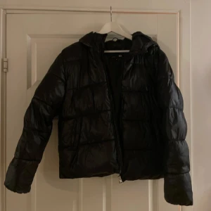 Svart pufferjacka från 157 - Snygg svart pufferjacka från 157 i storlek S. Jackan har en dragkedja framtill och är perfekt för kyligare dagar. Den är långärmad och har en klassisk pufferdesign som ger både stil och värme.