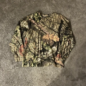 camo longsleeve  - Säljer en cool långärmad tröja med camouflage-mönster. Perfekt för utomhusaktiviteter eller som en stilren vardagströja. Tröjan har en normal passform och är gjord i ett bekvämt material. Står att den är L men sitter som M/S