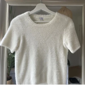 Vit fluffig t shirt - Säljer en supermjuk och fluffig vit topp med korta ärmar. Perfekt för en avslappnad stil och passar bra till både jeans och kjol. Toppen har en enkel design som gör den lätt att matcha med andra plagg.