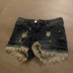 Jeansshorts med spetsdetaljer från Amisu - Snygga jeansshorts från Amisu med slitna detaljer och vacker spetskant. Perfekta för en avslappnad sommarlook. De har en klassisk femficksdesign och knappgylf.