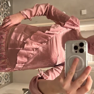 Rosa omlottblus med volangdetaljer - Säljer en söt rosa omlottblus med volangdetaljer. Blusen har långa ärmar och en elegant design som passar perfekt för både vardag och fest. 